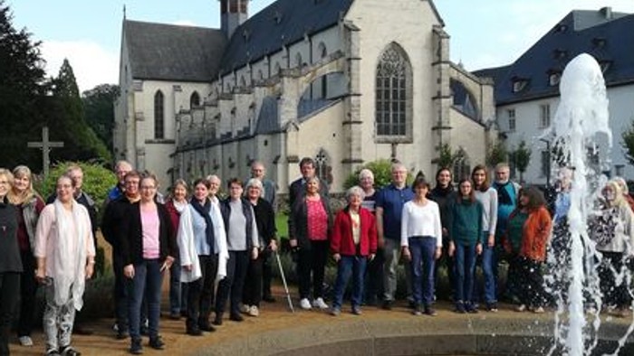 Eine Gruppe von Menschen steht vor einer Kirche mit einem Brunnen.