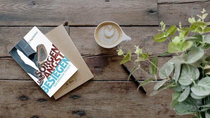 Buch, Kaffeetasse und Topfpflanze auf Holztisch