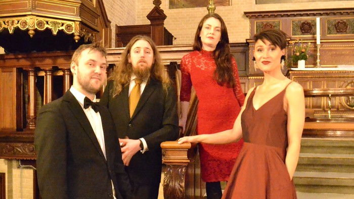 Fire mænd og en kvinde i festlige klæder står sammen i en kirke.