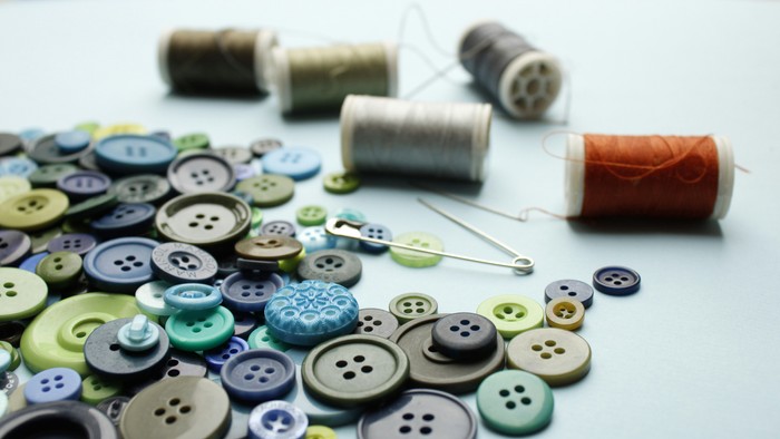 Viele Knöpfe und Spulen mit Garn auf weißer Oberfläche
