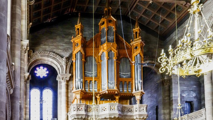 Orgue en bois doré suspendu dans une église avec vitraux et lustres.