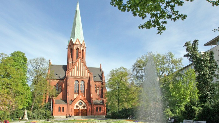 Ein rotes Kirche mit hohem Turm und ein Brunnen im Vordergrund