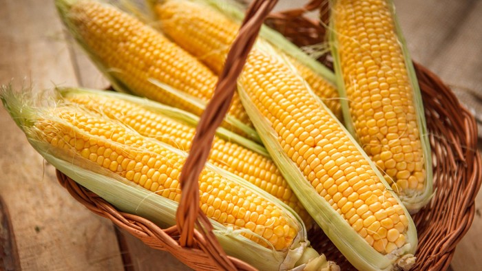 Korb mit frischen Maiskolben auf Holzoberfläche