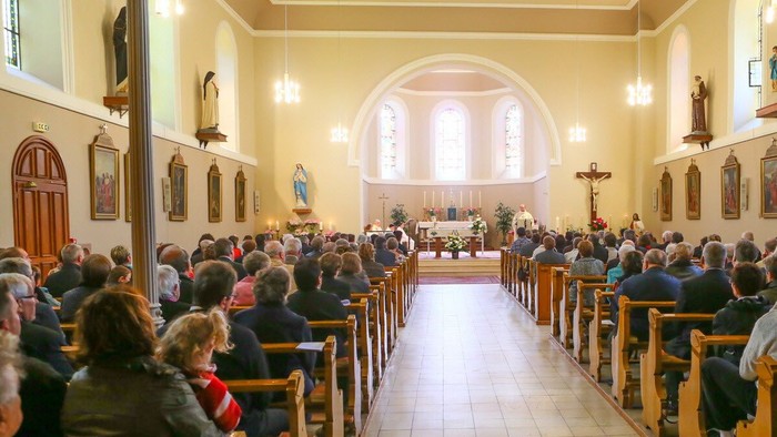Une église avec des fidèles assis dans des bancs, regardant vers l'autel.