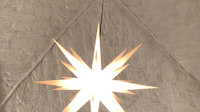 Ein großer, hell leuchtender Stern hängt von der Decke einer Kirche.