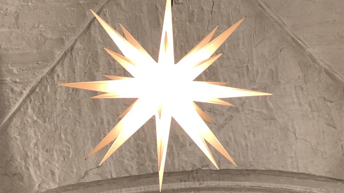Ein großer, hell leuchtender Stern hängt von der Decke einer Kirche.