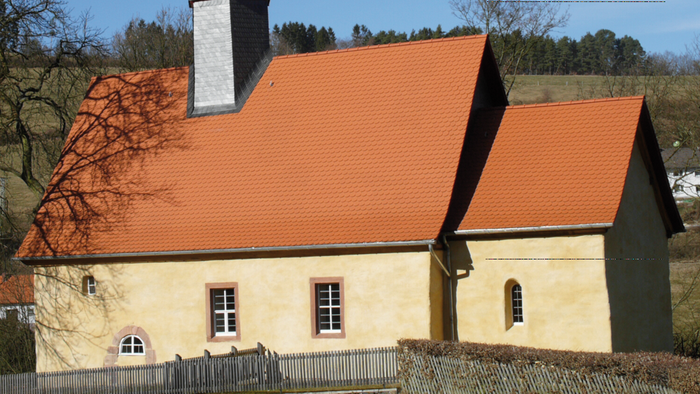 Kleine Kirche mit hohem Turm und rotem Dach in ländlicher Umgebung