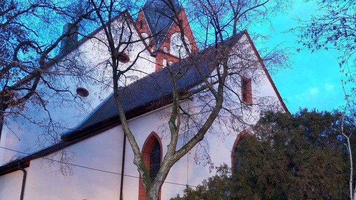 Kirchengebäude mit spitzen Fenstern und Bäumen vor blauem Himmel