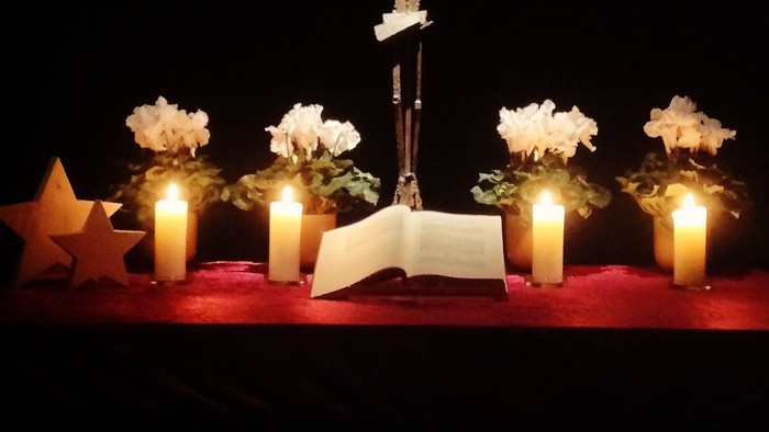 Ein Kreuz mit Knochen, umgeben von Kerzen und Blumen auf einem dunklen Hintergrund