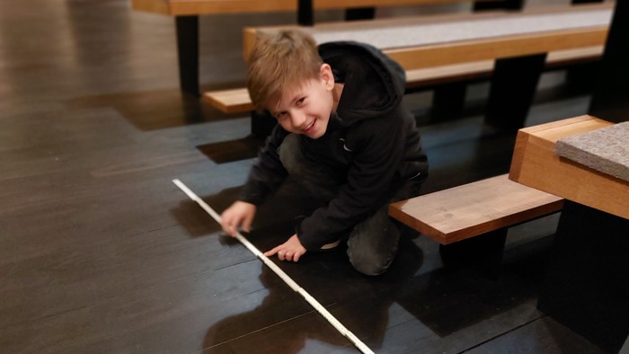 Junge kniet auf Boden und hält Lineal