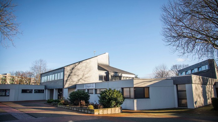 Modernes Gebäude mit flachem Dach und großen Fenstern, umgeben von Bäumen und Büschen