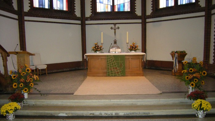 Innenraum einer Kirche mit Altar, Kerzen und Blumenarrangements