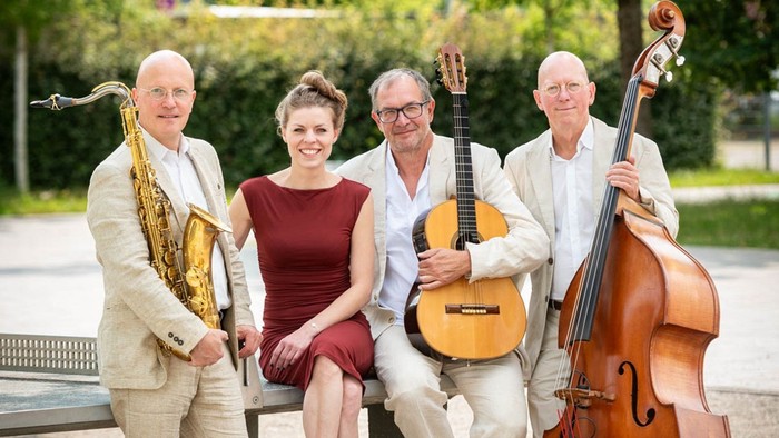 Vier Personen posieren mit Musikinstrumenten im Freien.