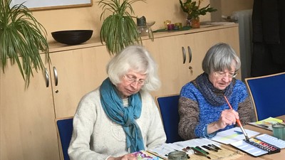 Zwei ältere Frauen sitzen an einem Tisch und schauen in ein Buch.