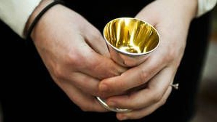 Hænder holder en lille guldfarvet kop.