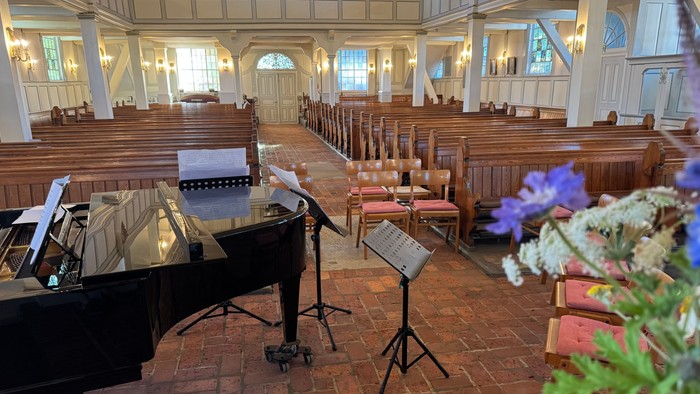 Elegante Kircheninnenausstattung mit einem Flügel, Kirchenbänken und Blumendekorationen auf einem Ziegelboden.