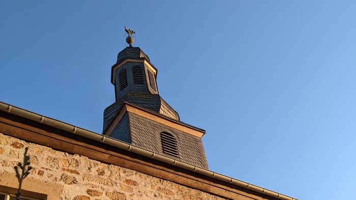 Steinerne Kirche mit hohem Kirchturm und Kreuz vor klarem, blauem Himmel.