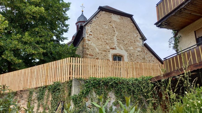 Steingebäude mit Holzzaun und Grünflächen.