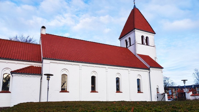 En hvid kirke med røde tag og tårn foran græsplæne