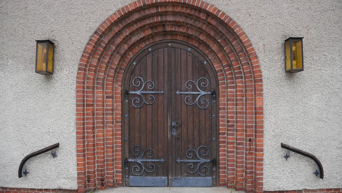 Elegante bogenförmige Holztür, gerahmt von rotem Backstein und flankiert von wandmontierten Laternen.