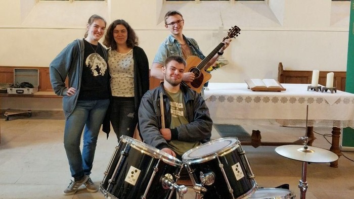 Eine Gruppe von Musiker:innen mit Instrumenten in einer Kirche mit bunten Glasfenstern.