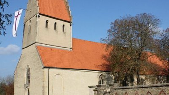 Kirchengebäude mit hohem Turm und roter Flagge vor blauem Himmel