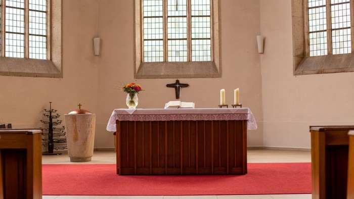Ein Altar in einer Kirche mit Kerzen und Blumen, vor einem großen Fenster