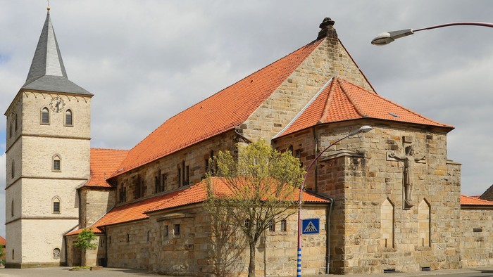 Altes Steinhaus mit hohem Turm und rotem Dach, daneben ein Baum und eine Straßenlaterne