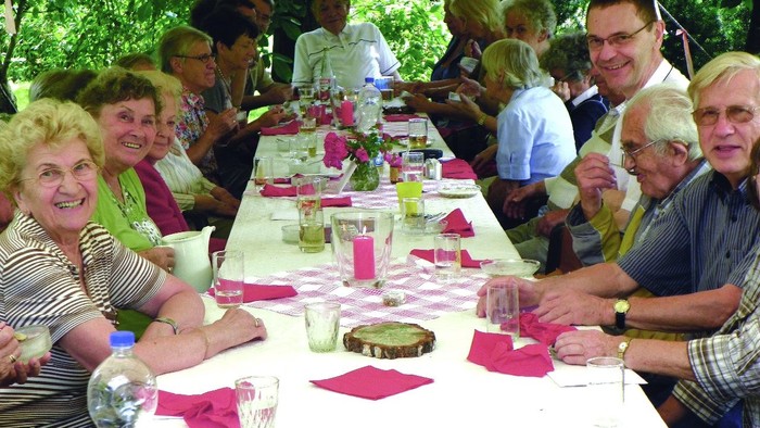 Eine Gruppe älterer Menschen sitzt an einem festlich gedeckten Tisch im Freien.