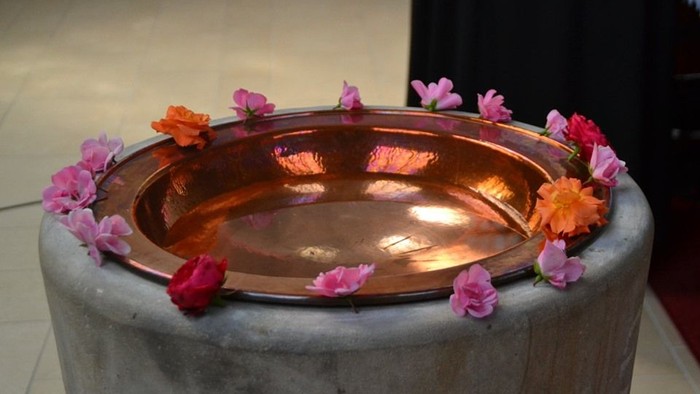 Eine Kupferschale auf einem Steinsockel mit bunten Blumen umrandet