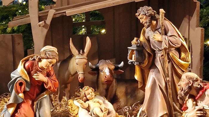 Eine Krippe mit Figuren und einem Engel, umgeben von Weihnachtsbeleuchtung