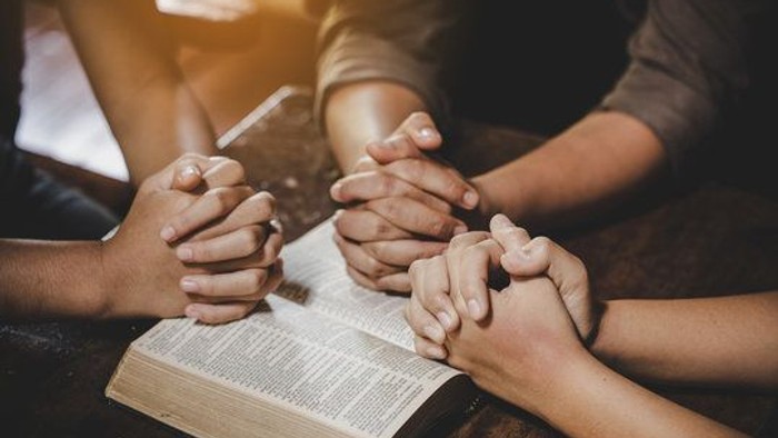 Hands clasped together over an open book, suggesting prayer or unity.