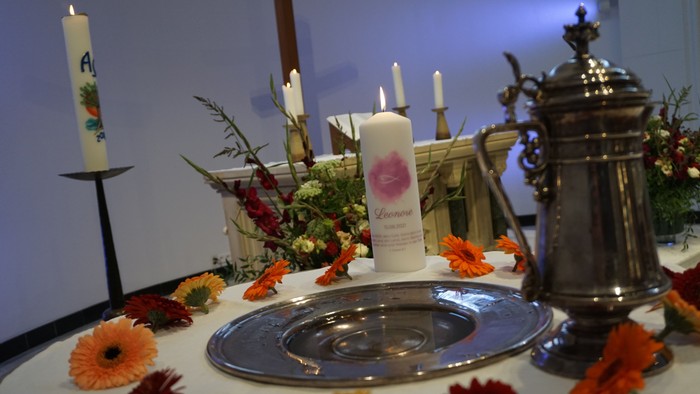 Tisch mit Kerzen, Blumen und einem Metallbehälter