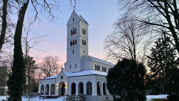 Weiße Kirche mit hohem Kirchturm, umgeben von Schnee und Bäumen.