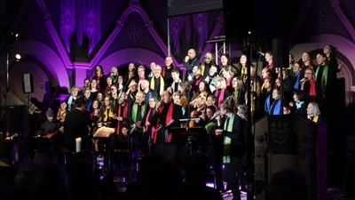 Ein großer Chor tritt auf einer Bühne auf, begleitet von einem Orchester.