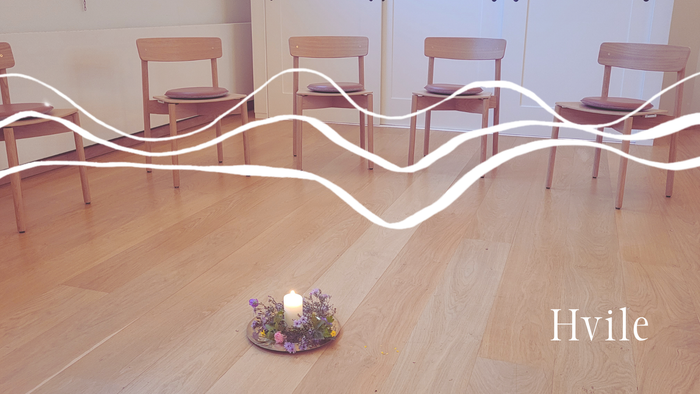 Minimalistisk værelse med træstole arrangeret i en halvcirkel omkring et lille blomsterlys-centerstykke.
