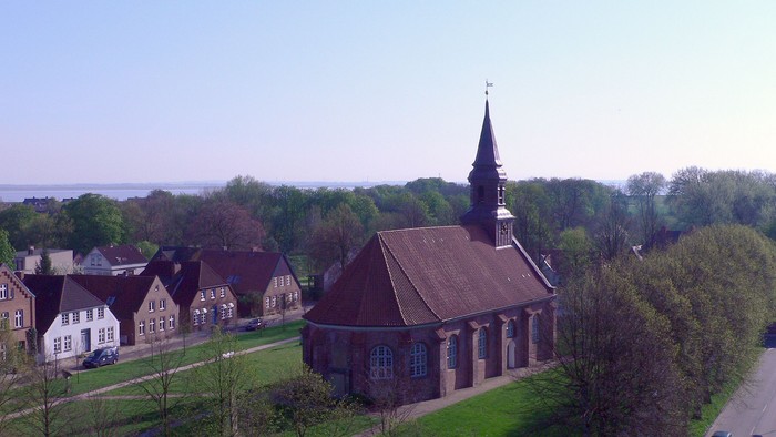 Kirche mit hohem Turm inmitten von Grünflächen und Häusern.