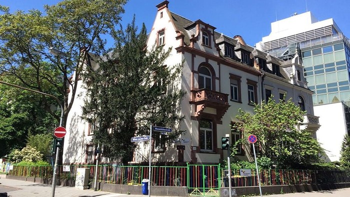 Historisches Gebäude, umgeben von Grünflächen in städtischer Umgebung mit modernen Hochhäusern im Hintergrund.