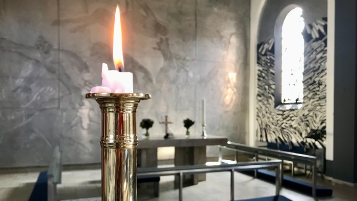 En lysende stearinlys i guldfarvet lysestage i kirke.