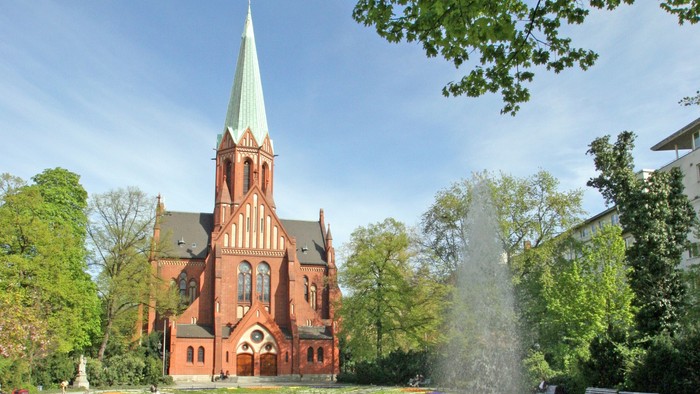Ein rotes Kirche mit hohem Turm und ein Brunnen im Vordergrund