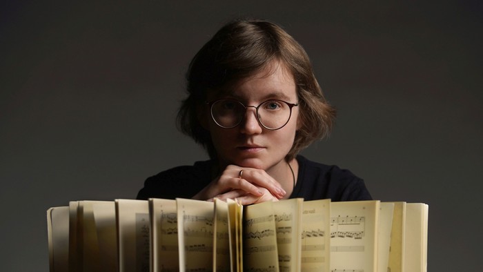 Eine Frau mit Brille lehnt an einem Stapel Bücher.