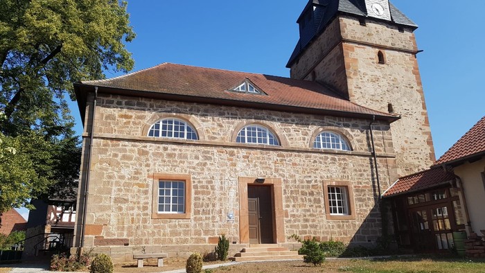 Steingebäude mit Rundbogenfenstern und hohem Uhrturm.