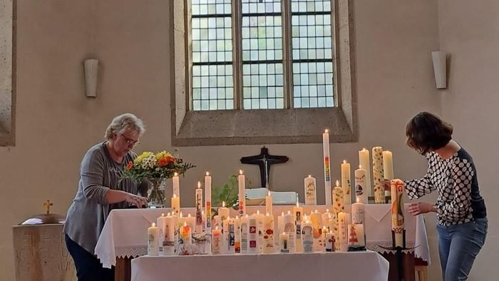 Zwei Personen zünden Kerzen an einem Gedenkaltar in einer ruhigen Kirche mit bunten Glasfenstern an.
