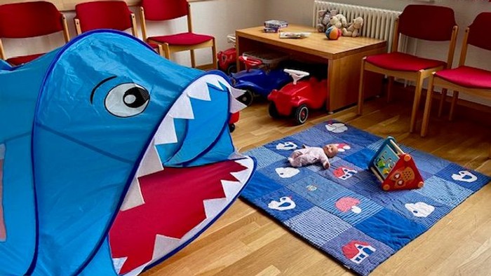 Im Kinderzimmer steht ein blaues Haifisch-Zelt neben einem blauen Teppich mit Spielzeug.