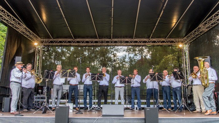 Eine große Blaskapelle spielt auf einer Bühne unter einem Zelt.