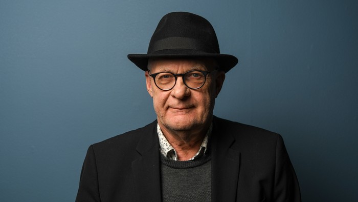 En ældre mand med briller og fedora, smilende mod kamera.
