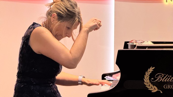 A woman in an elegant dress plays piano with a focused expression during a performance.