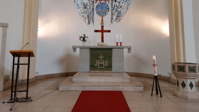 Die Kirche zeigt einen Altar mit Kreuz und Kerzen, einen Taufstein und eine Kanzel
