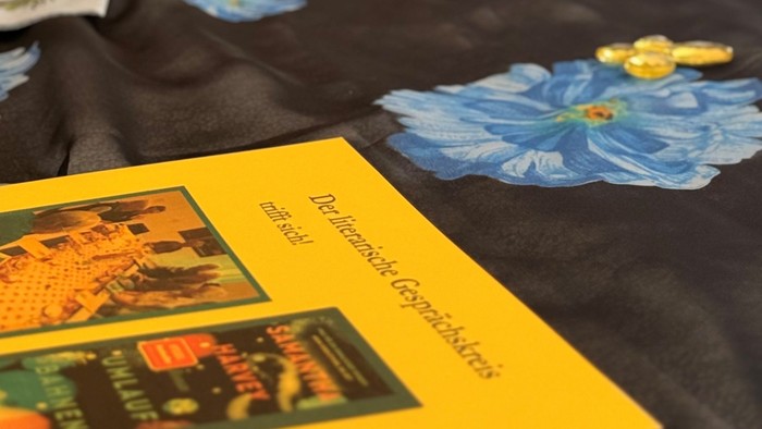 Mit blauen Blumenmustern verzierter Tisch und gelben Heftchen mit Kunstwerken auf einer schwarzen Tischdecke.