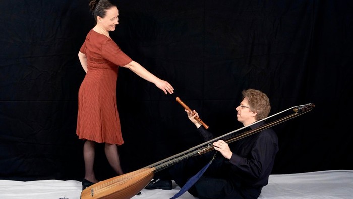 Eine Frau in rotem Kleid reicht einem Mann eine große Laute.